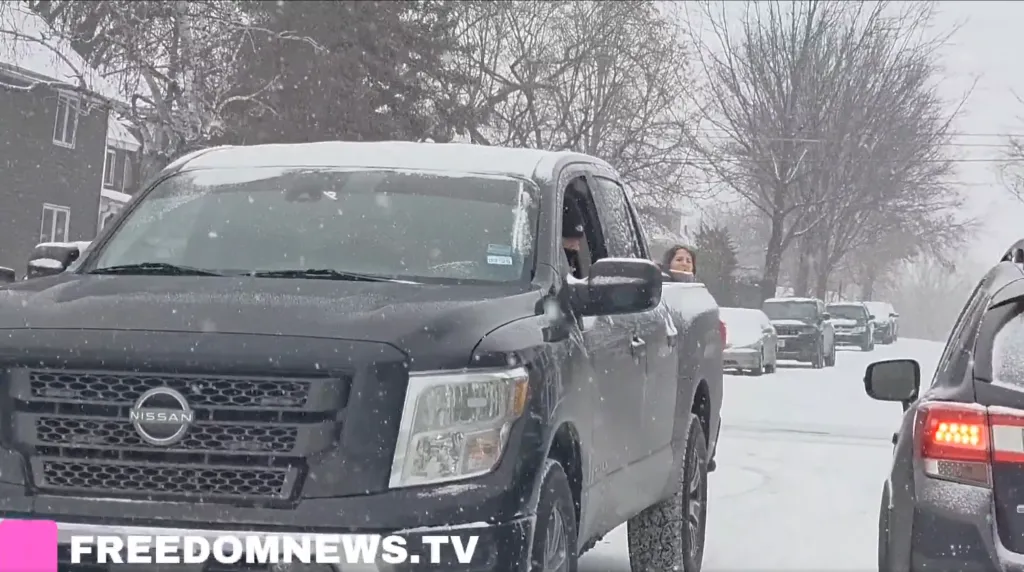 A black Nissan Titan pickup truck on a snow-covered street with a woman looking out the back window.